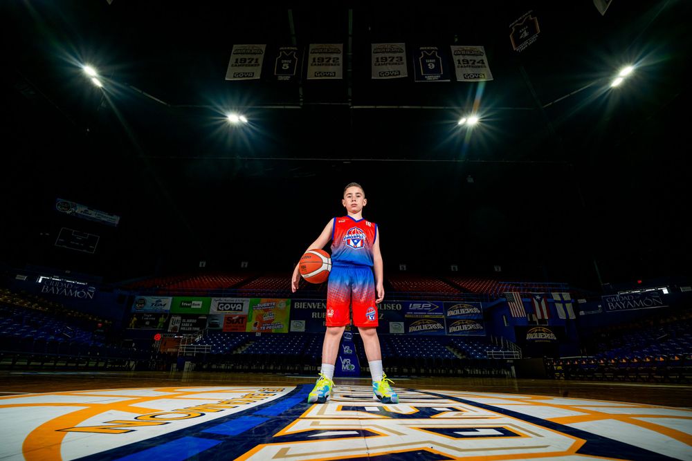 Basketball player standing on illuminated court logo under dramatic lighting.