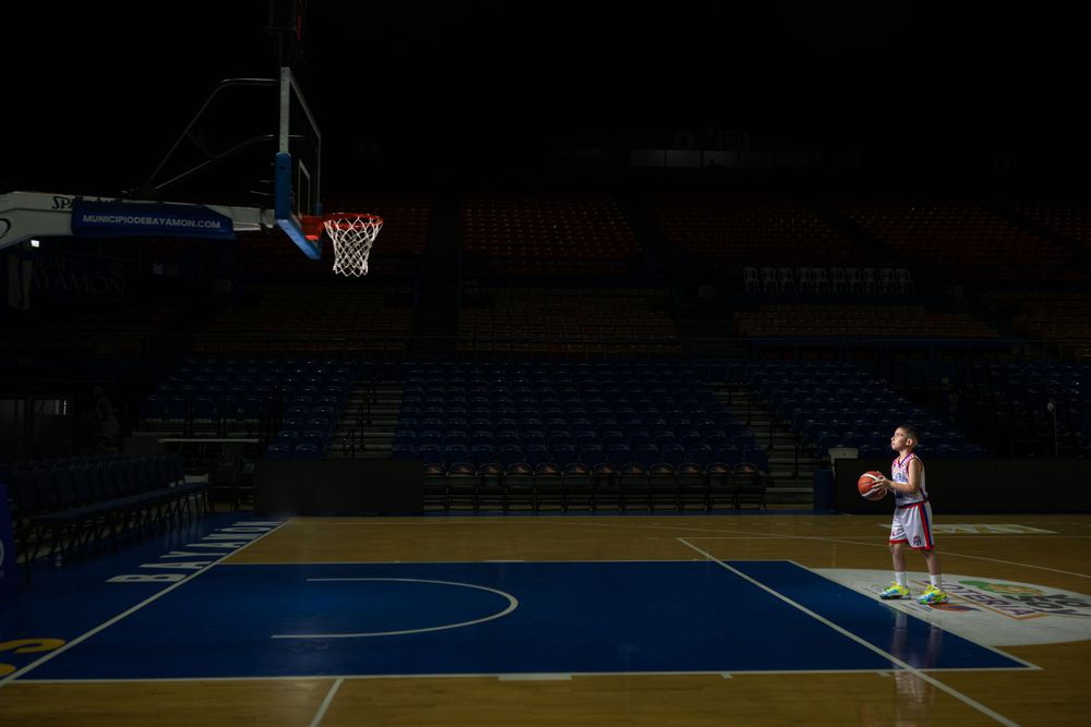 Solo basketball player standing on darkened court under spotlight.
