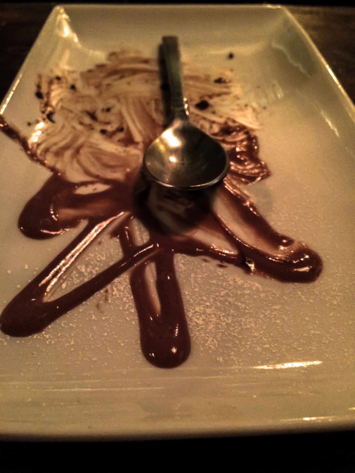 A plated dessert with chocolate sauce artfully drizzled on a white plate with a spoon.