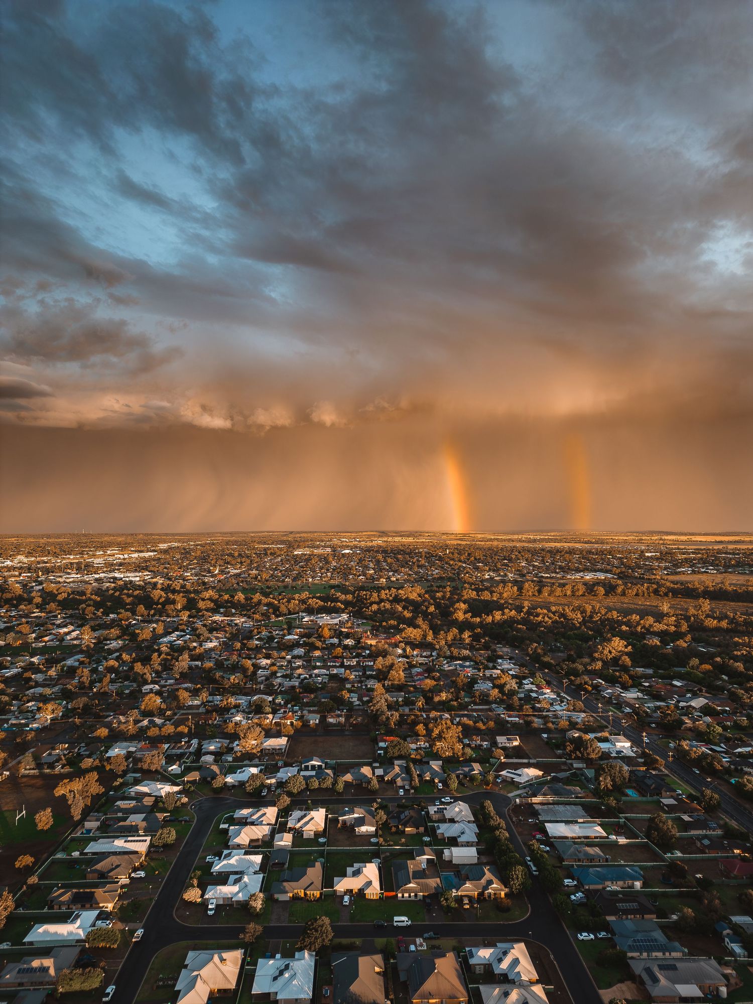 Dramatic sunset cityscape with orange sky and light pillars reflecting over suburban rooftops.