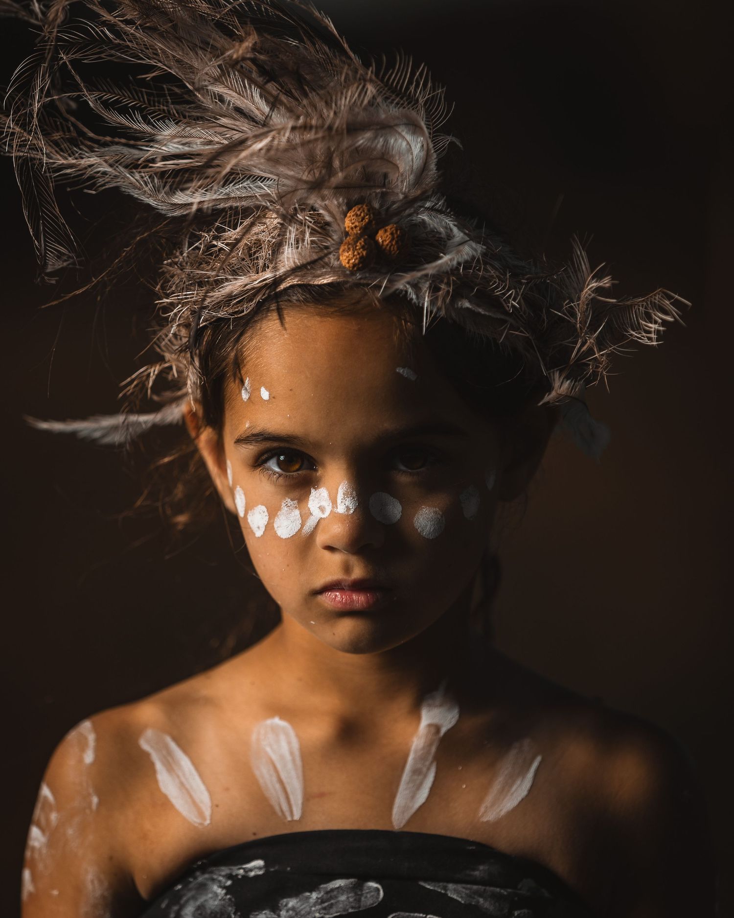 Artistic portrait with tribal face paint and dramatic lighting against dark background.