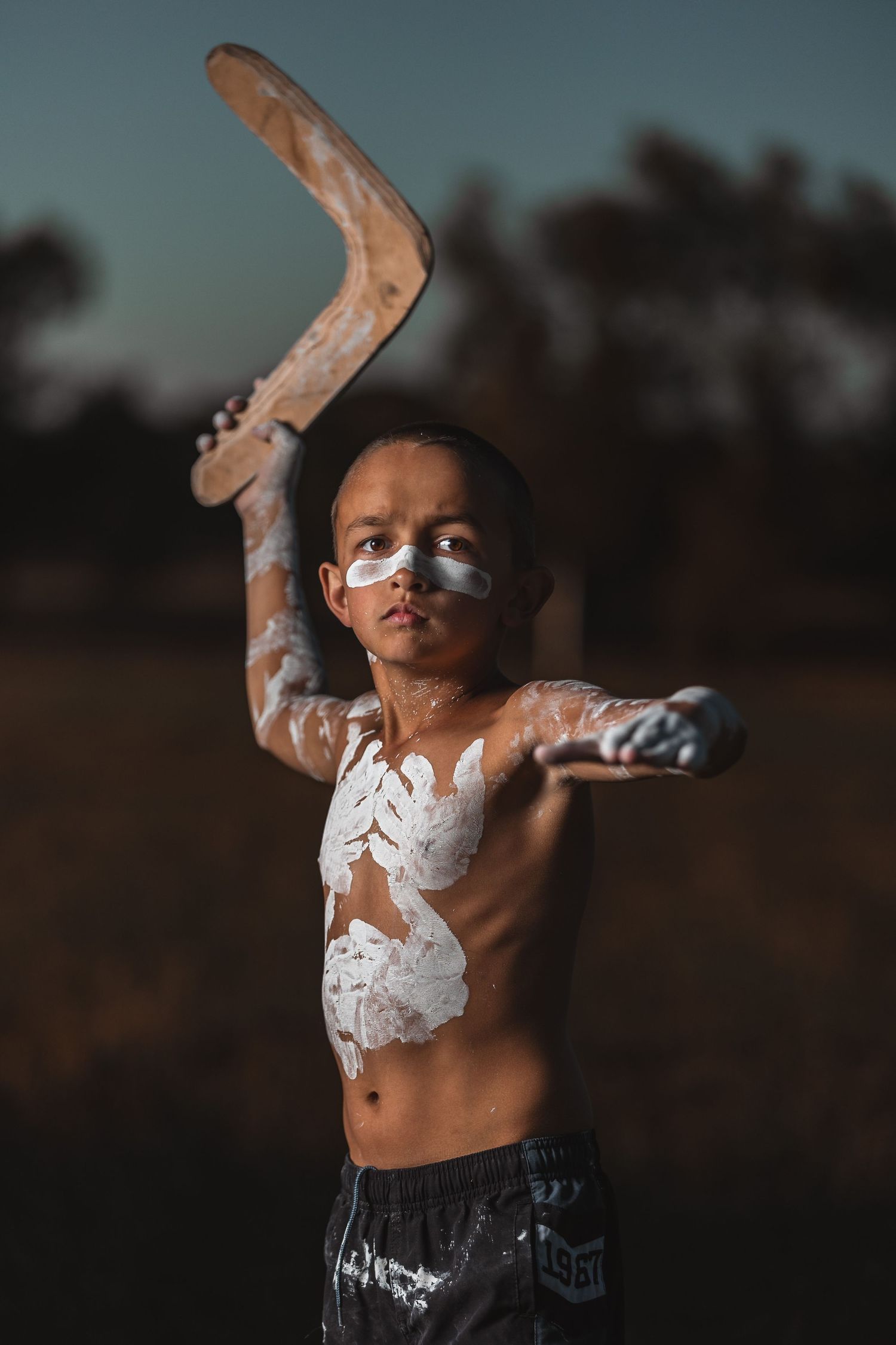 Dramatic outdoor portraits with white tribal body paint against evening sky.