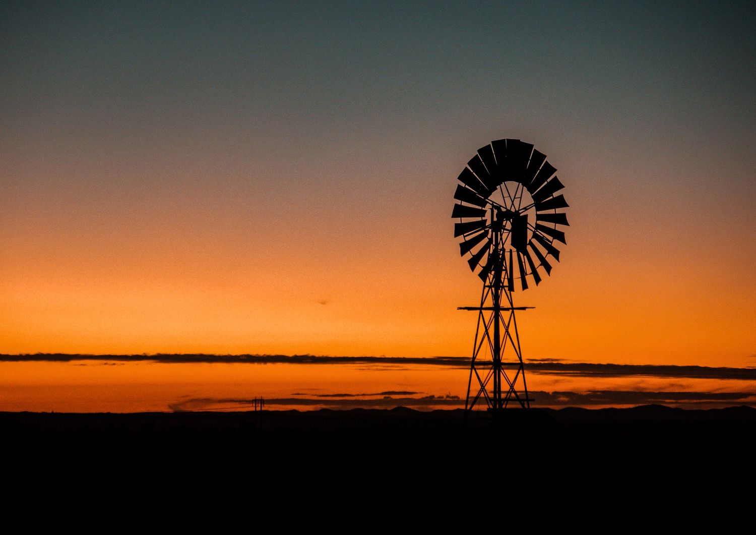 Windmill silhouetted against an orange sunset sky over flat Australian outback terrain.