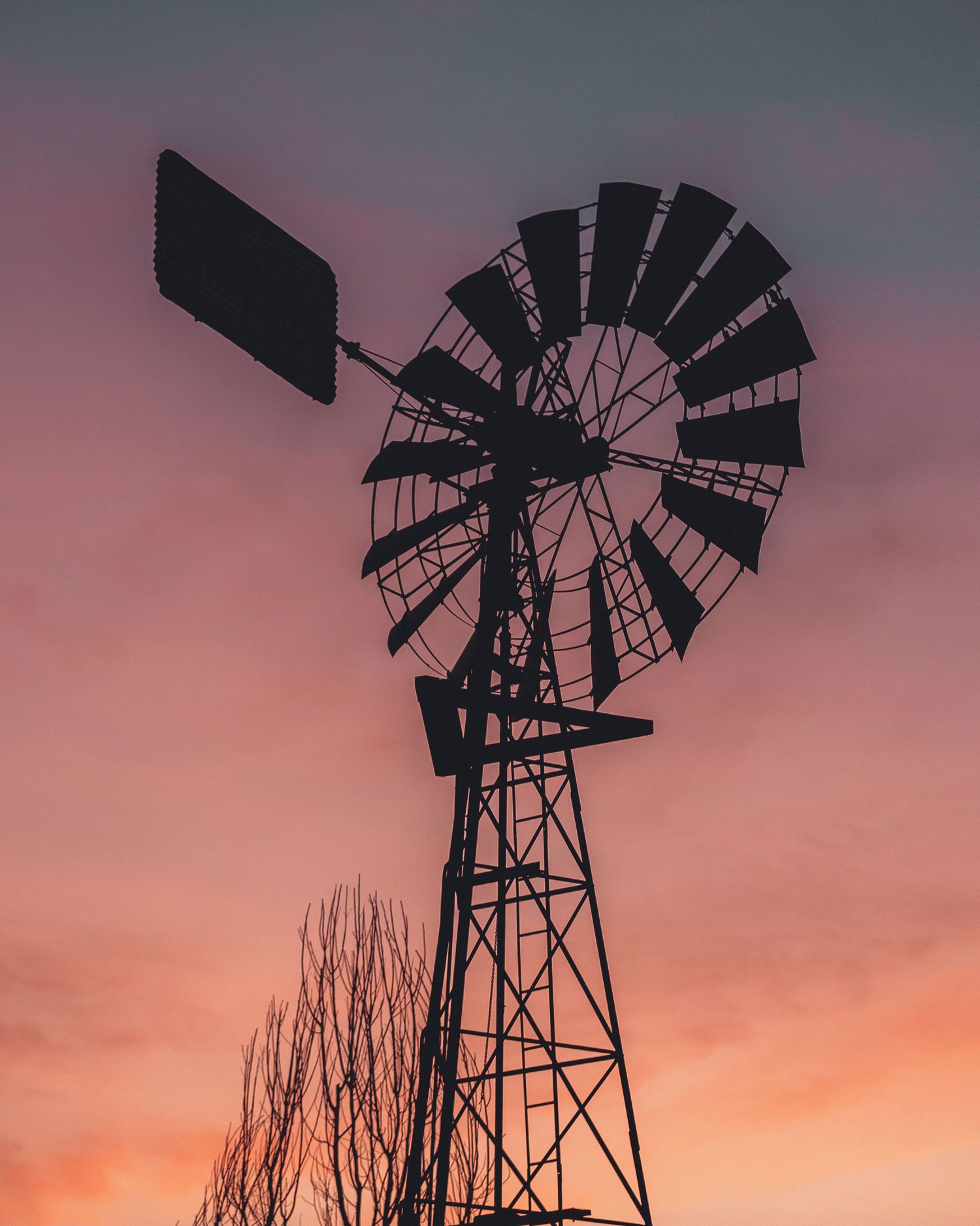 Silhouette of a windmill against a pink and orange sunset sky creating a dramatic rural landscape.