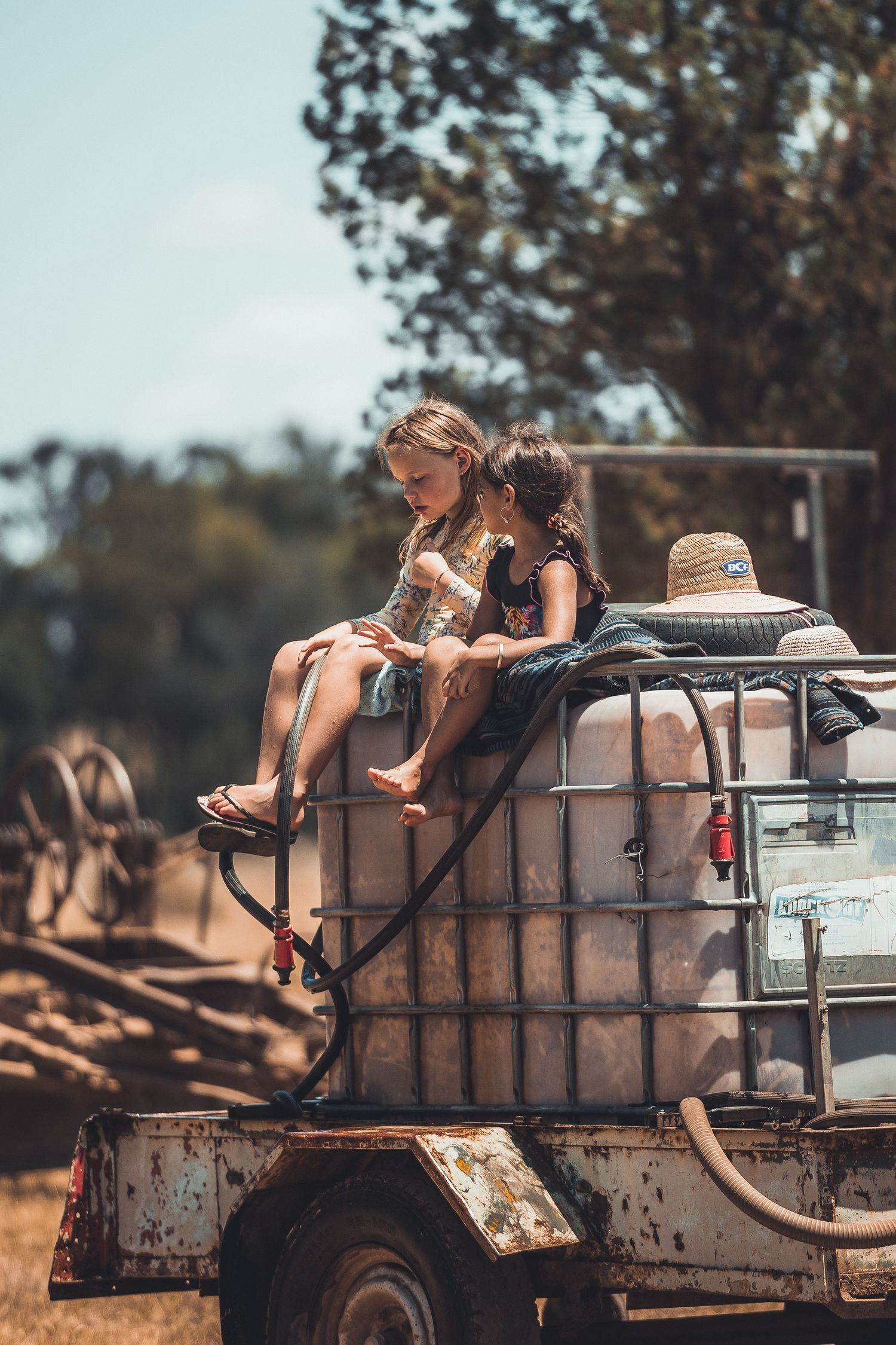 Vintage water tank truck with children sitting on top in a rural setting.