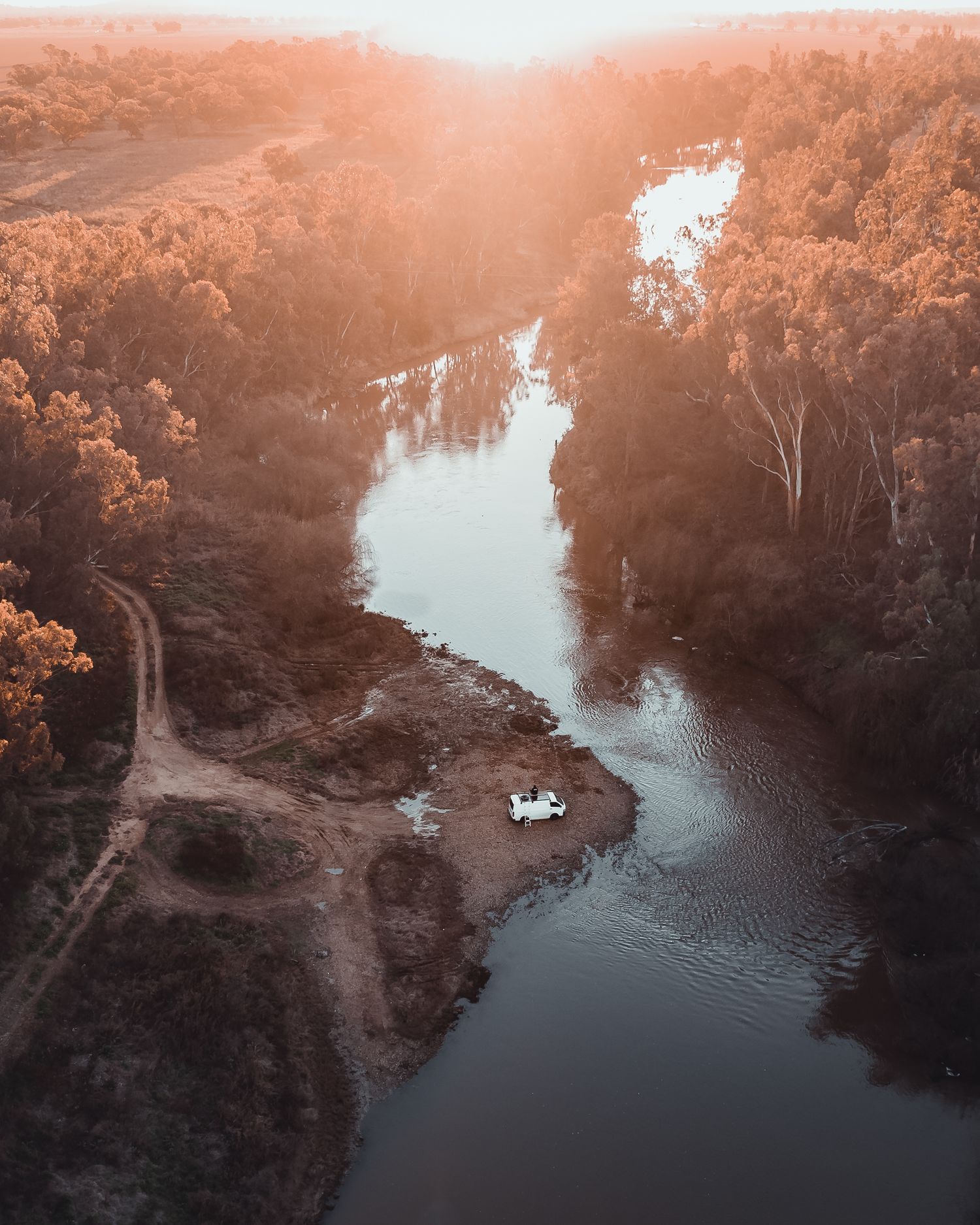 Aerial view of a winding river through autumn forest landscape at golden hour.