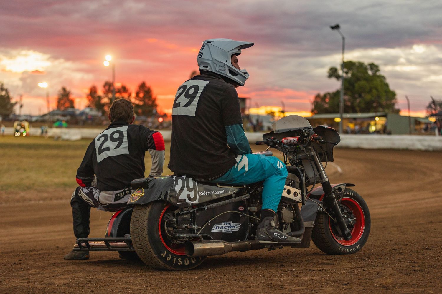 Vintage motorcycles lined up at sunset on a dirt track for racing competition.