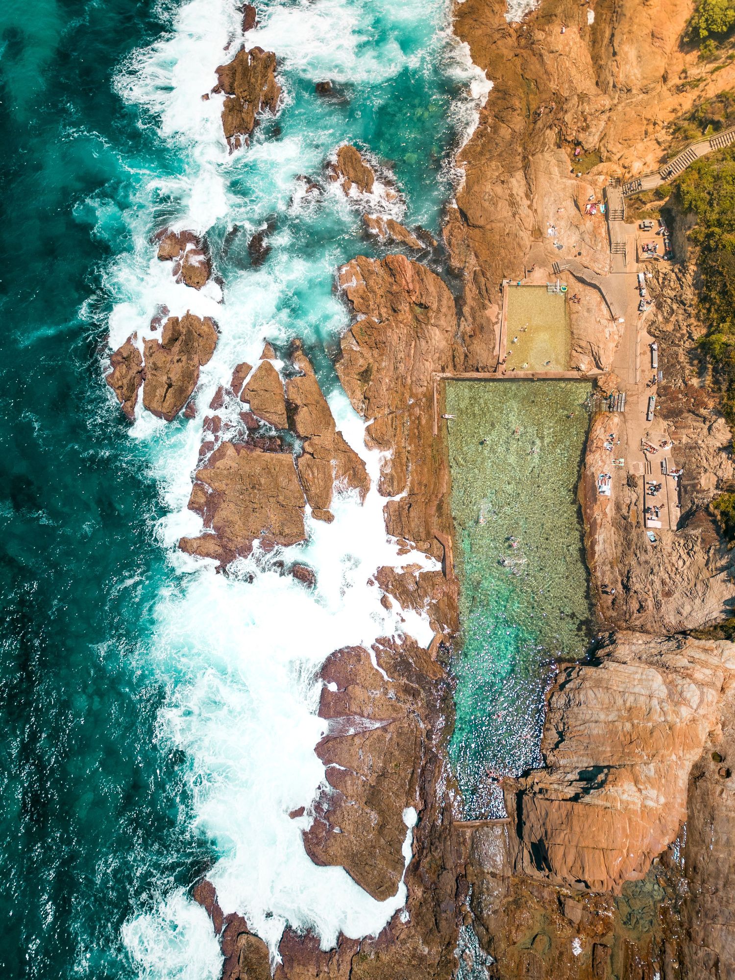 Aerial view of rugged coastline where turquoise waters meet rocky orange cliffs.