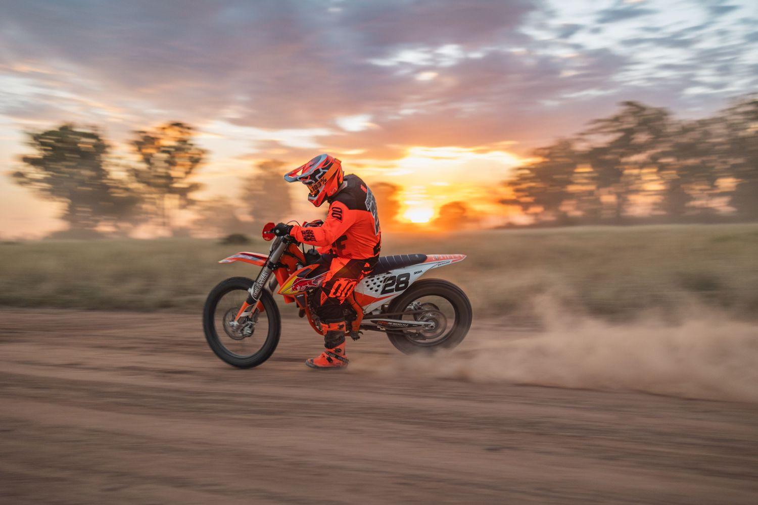 Motocross rider on orange dirt bike jumping at sunset creating dramatic action shot.