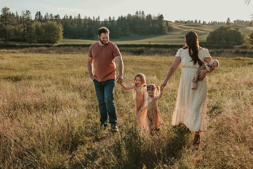 family of five in spokane holding hands and walking all wearing earth tone outfits in open field and rolling hills