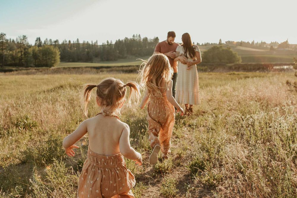 family of five in spokane two little girls running towards mom and dad all wearing earth tone outfits