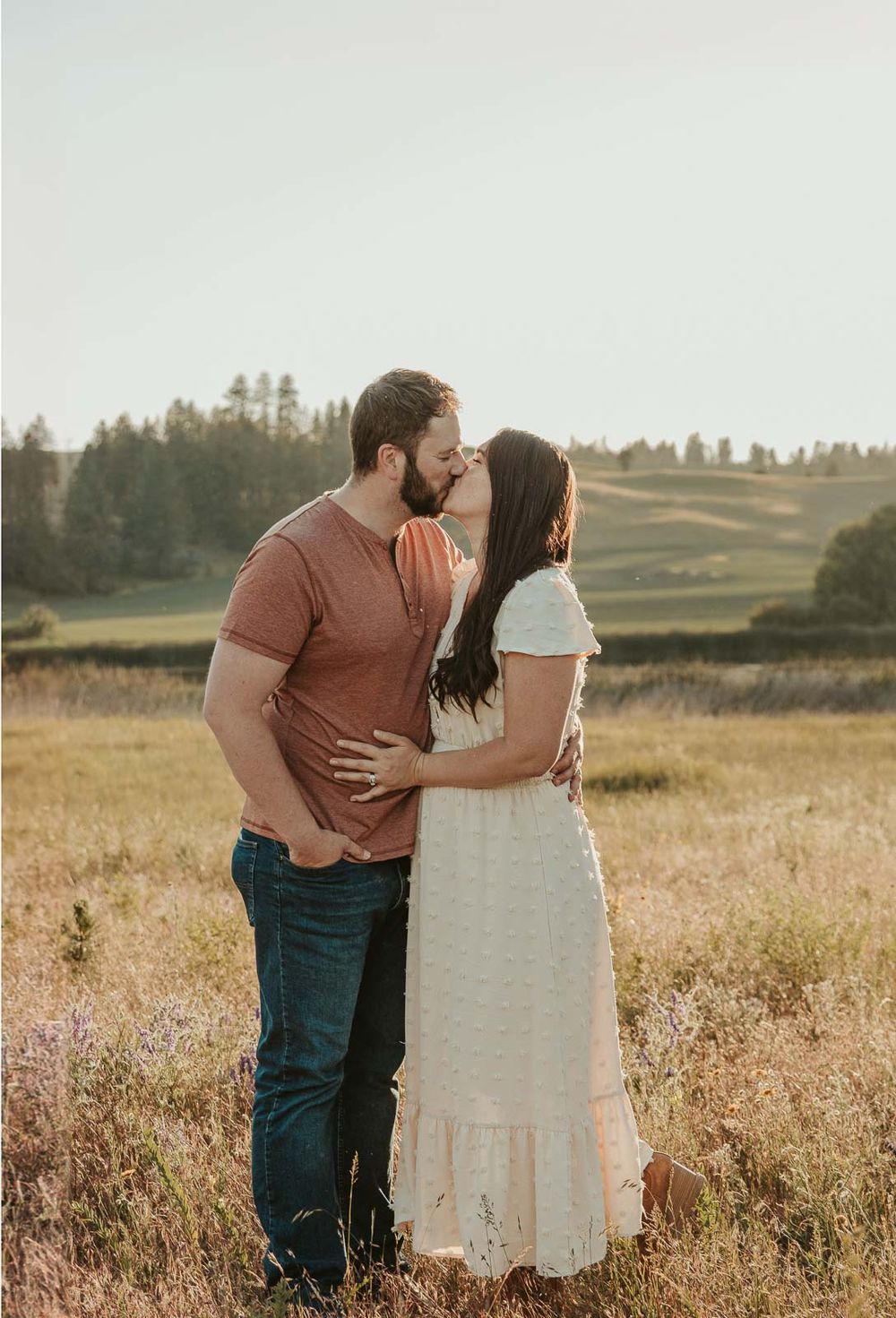 man dressed in brown shirt with woman in white kissing each other in a spokane open wildflower field