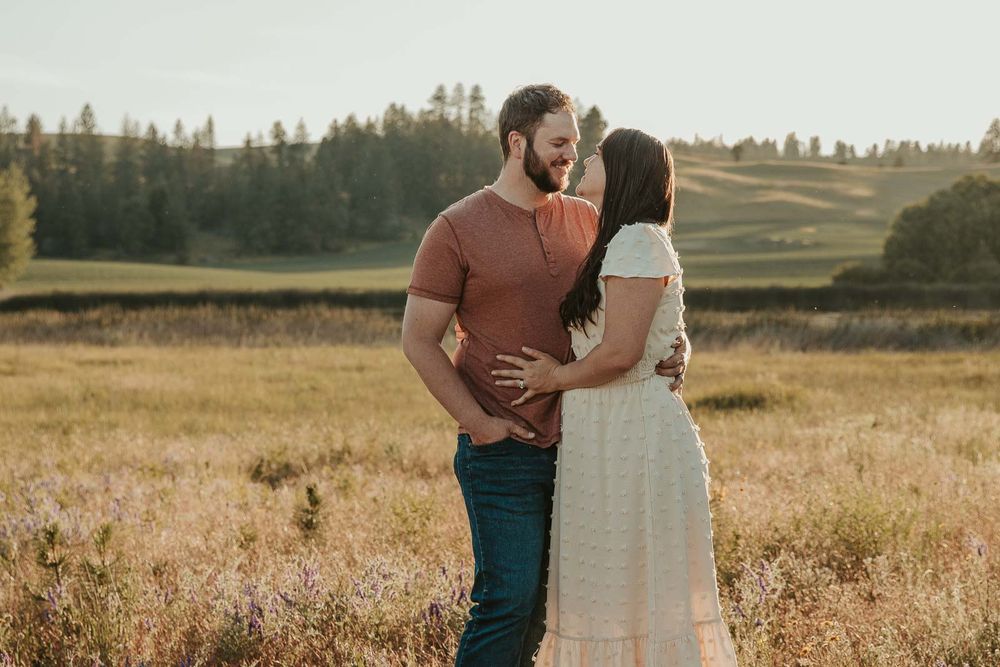man dressed in brown shirt with woman in white looking at each other in a spokane open wildflower field