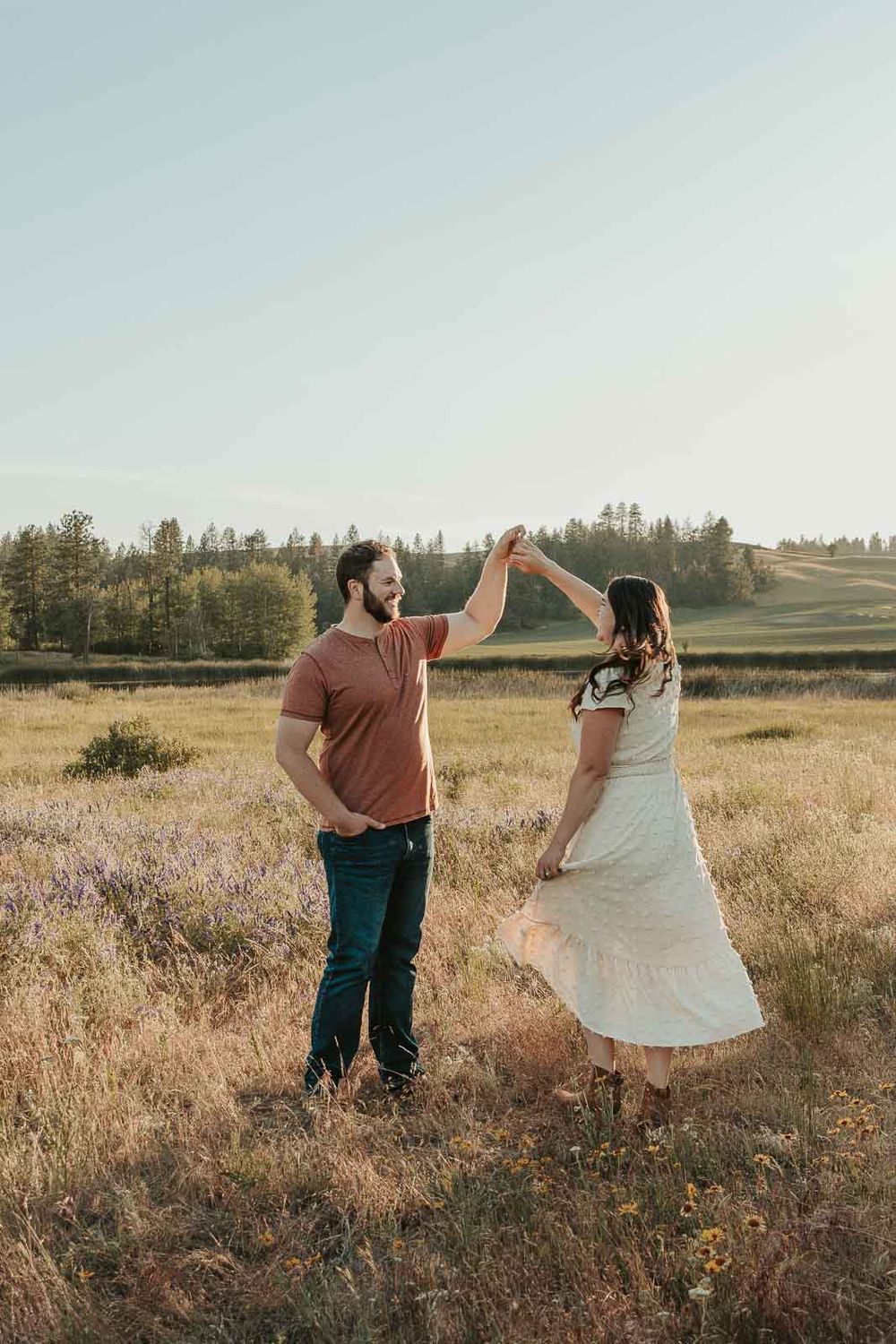 man dressed in brown shirt with woman in white dress dancing in a spokane open wildflower field
