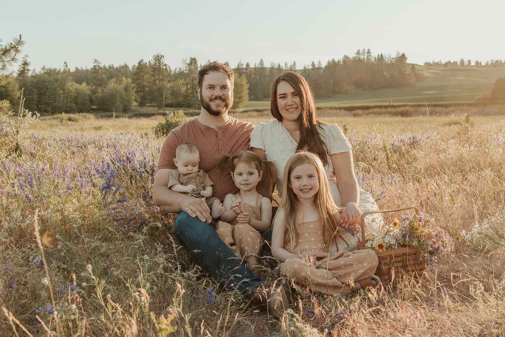 spokane family sitting in a flower field dressed in earth tones smiling at the camera