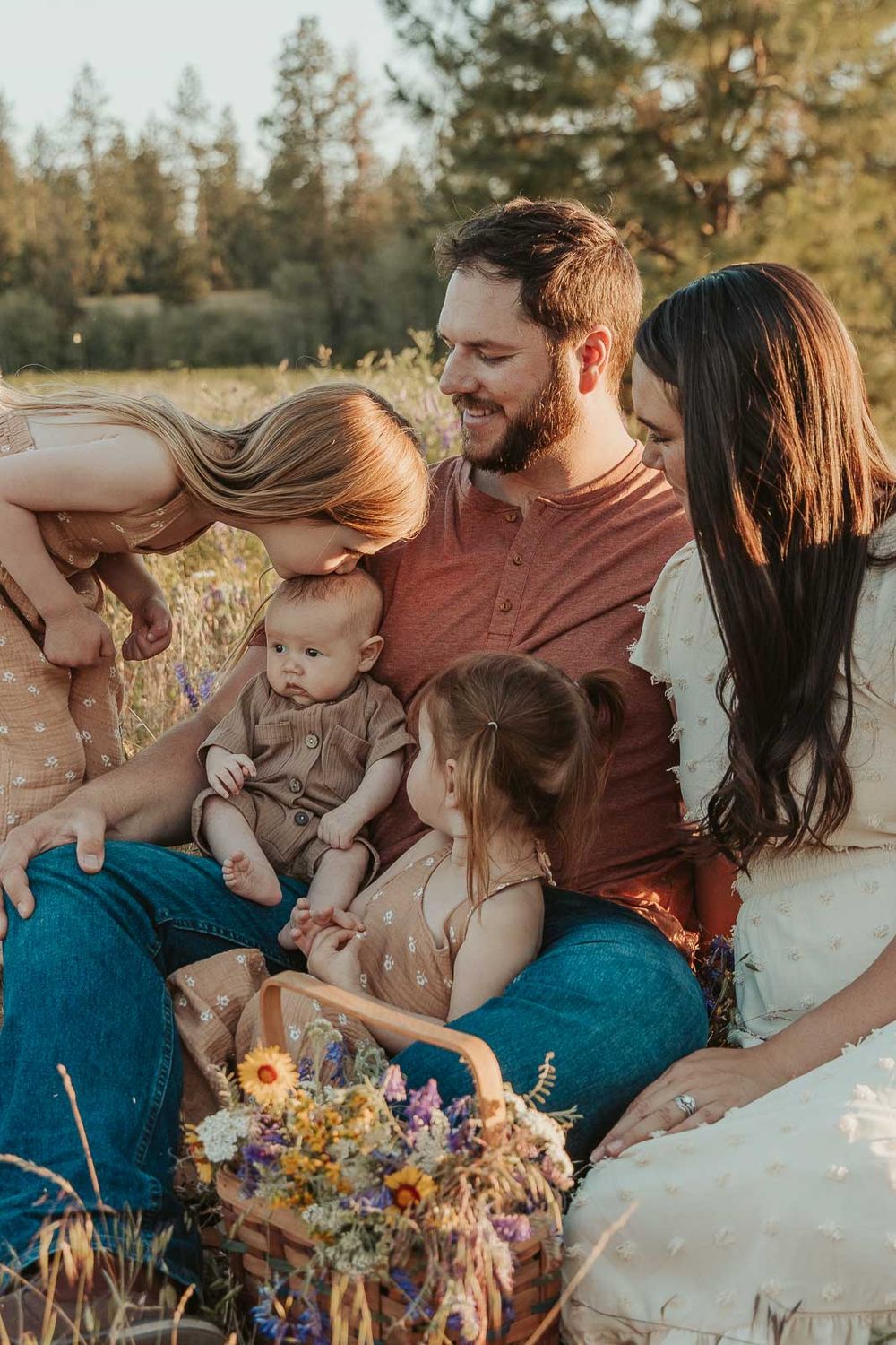 spokane family sitting in a flower field big sister is kissing baby brother on the head all are smiling
