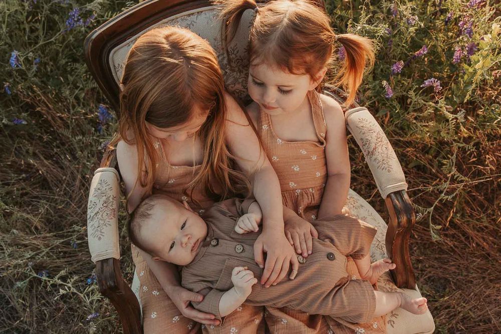 two red haired girls holding baby brother sitting in a spokane flower field
