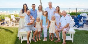 Large multigenerational family group poses together on green lawn with ocean view in background.