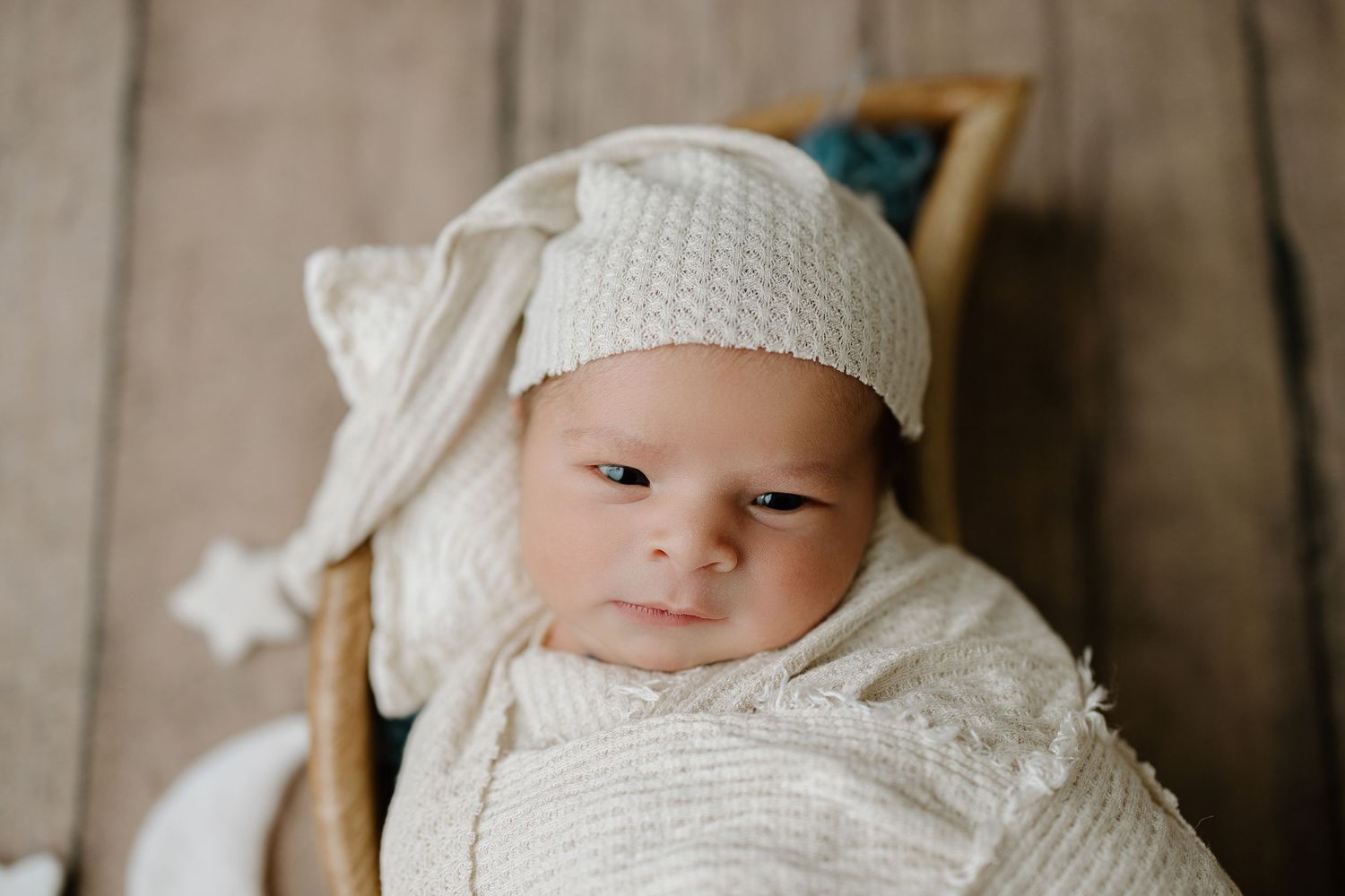 Baby wearing white knit bonnet and wrap during newborn photo session.