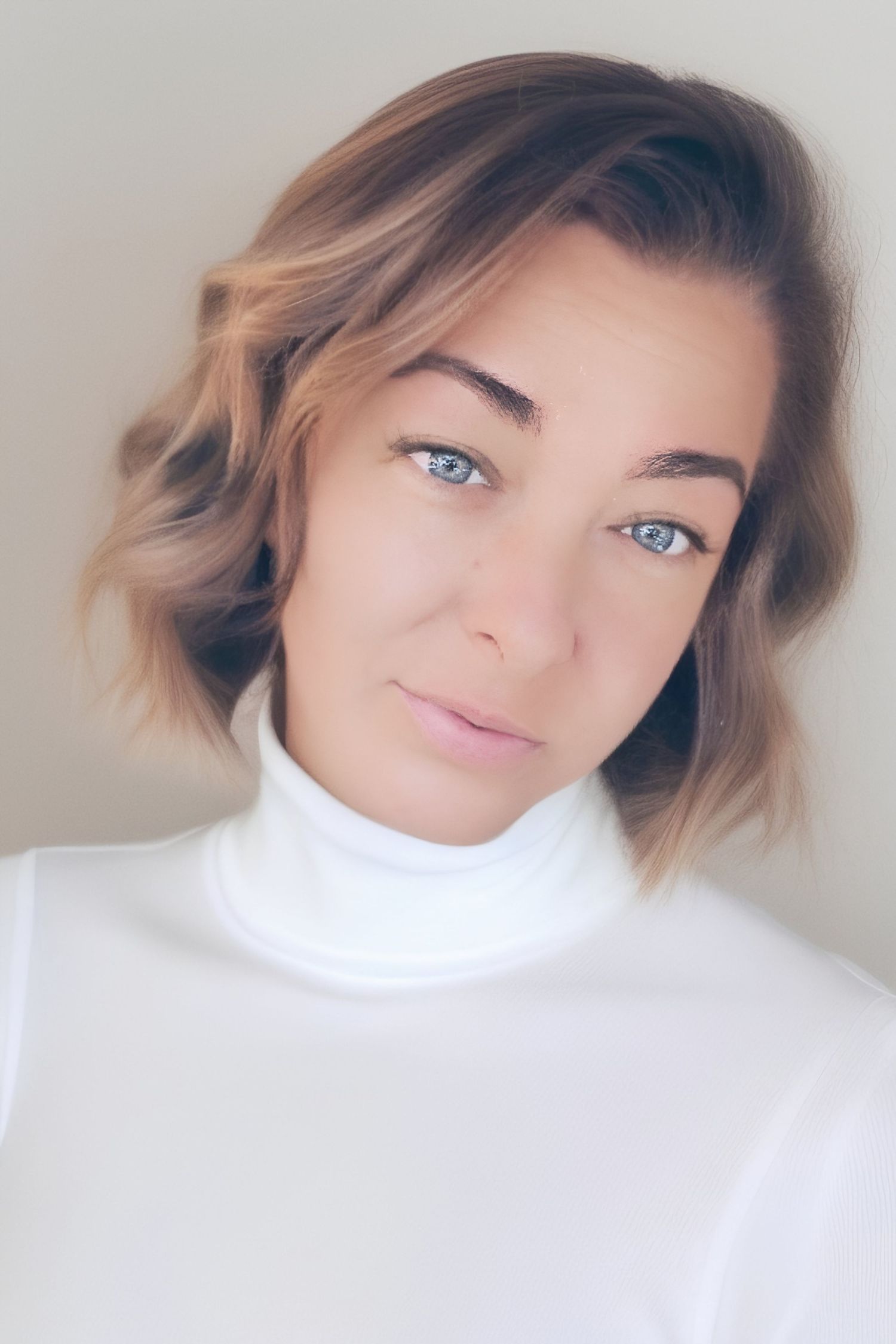 Close-up portrait of someone wearing a white turtleneck sweater with soft lighting and natural wavy hair.