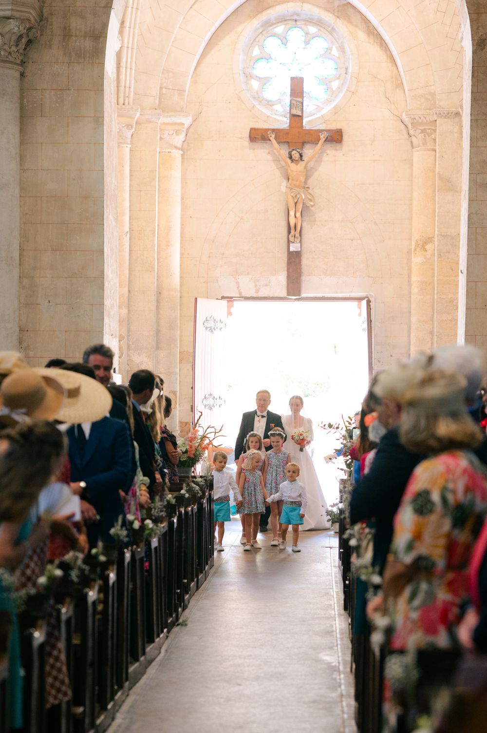 Wedding ceremony takes place inside a historic church with arched ceilings and crucifix, as guests watch from wooden pews.