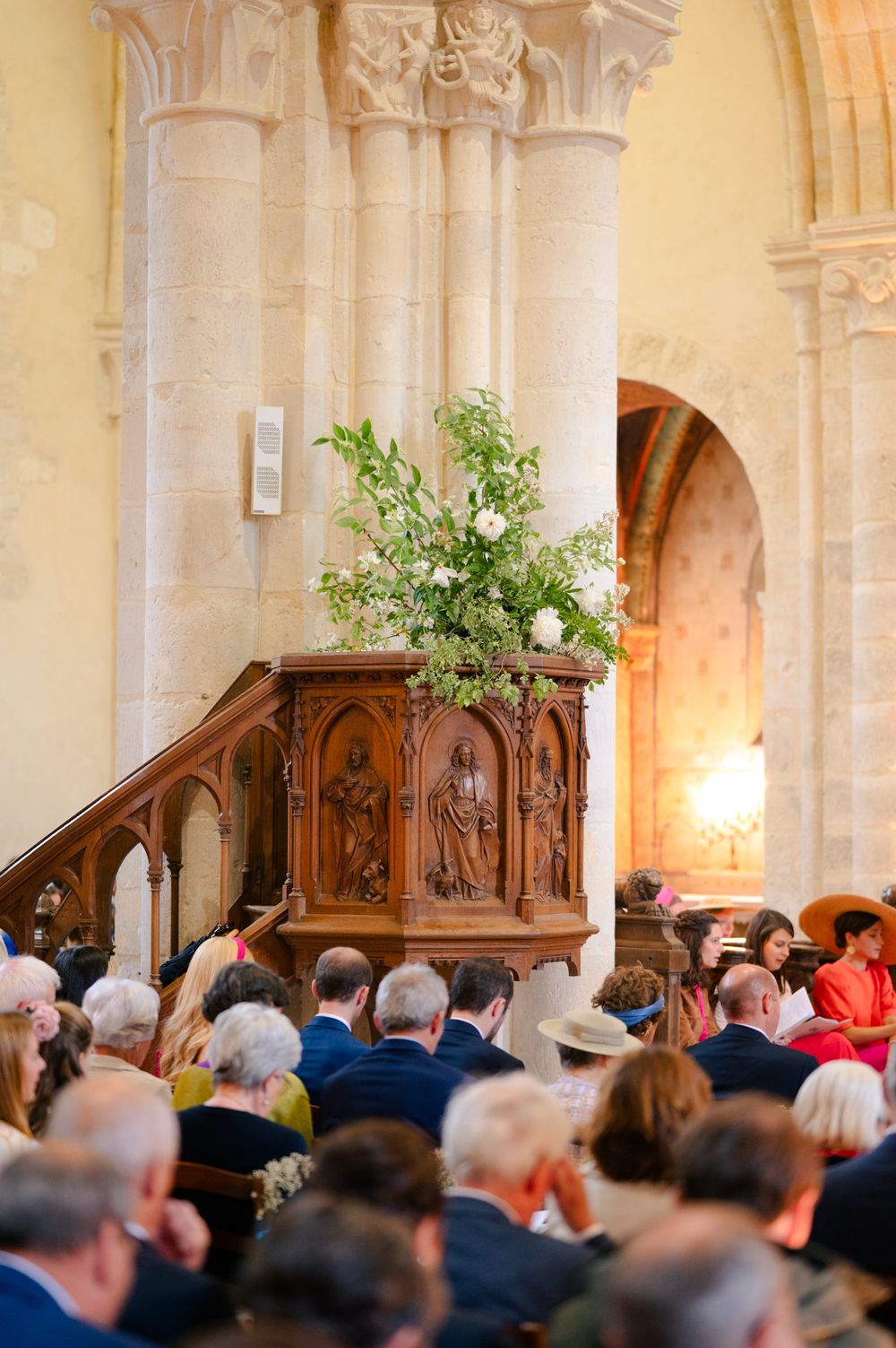 A decorated wooden pulpit adorned with floral arrangements stands in a church filled with congregation members.