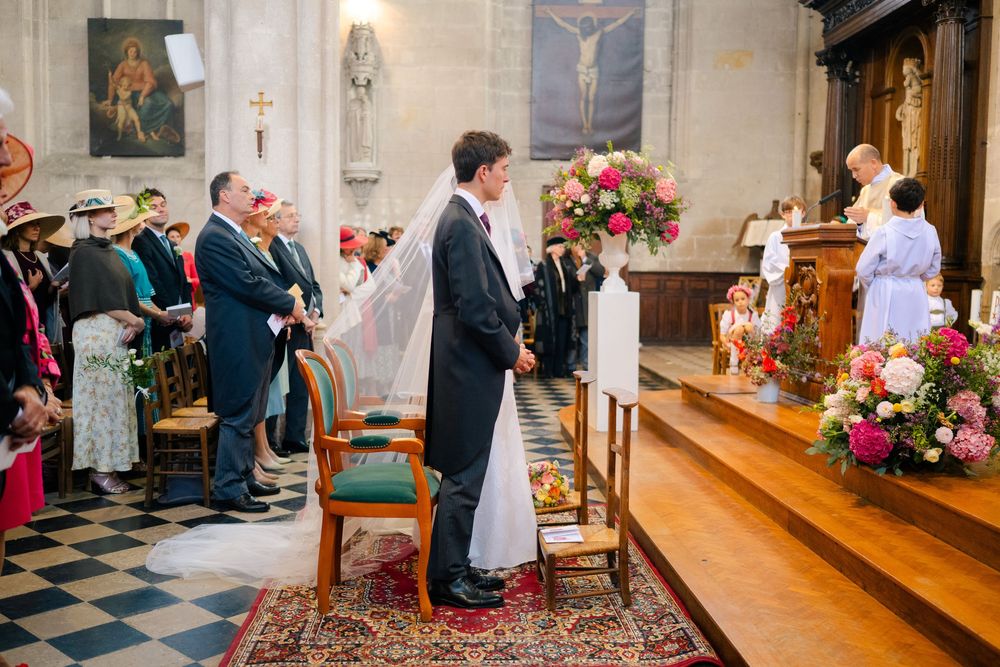 A couple stands at the altar during their traditional Catholic church wedding ceremony with floral decorations and guests.