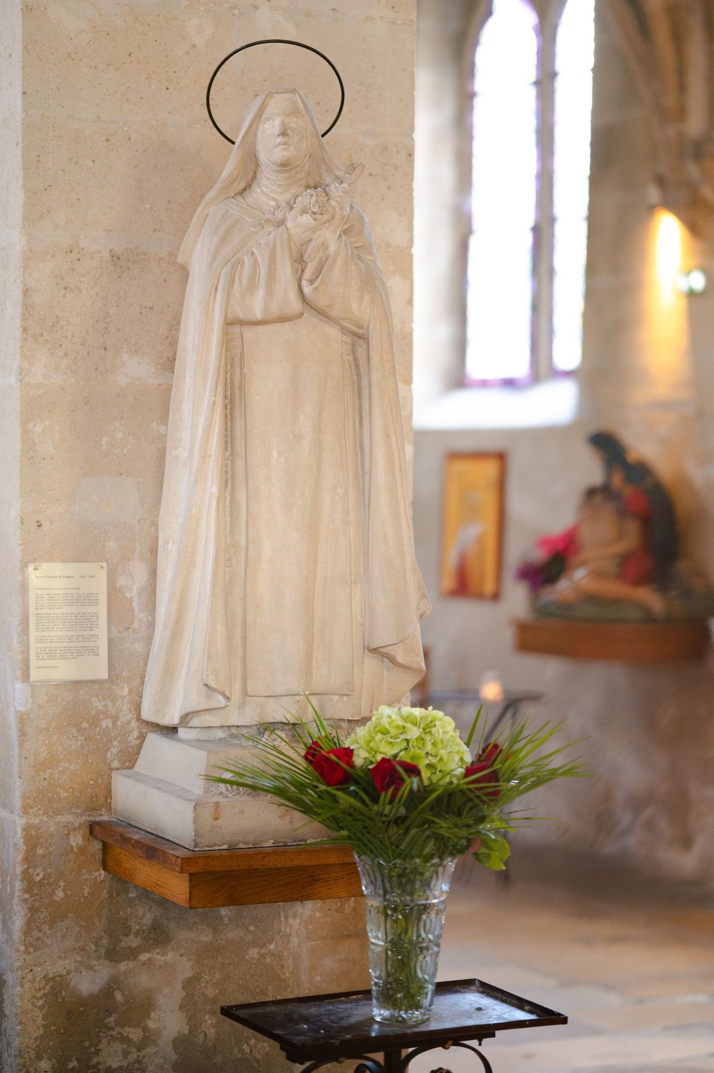 White marble statues and sculptures displayed in a church interior with stone walls and stained glass windows.