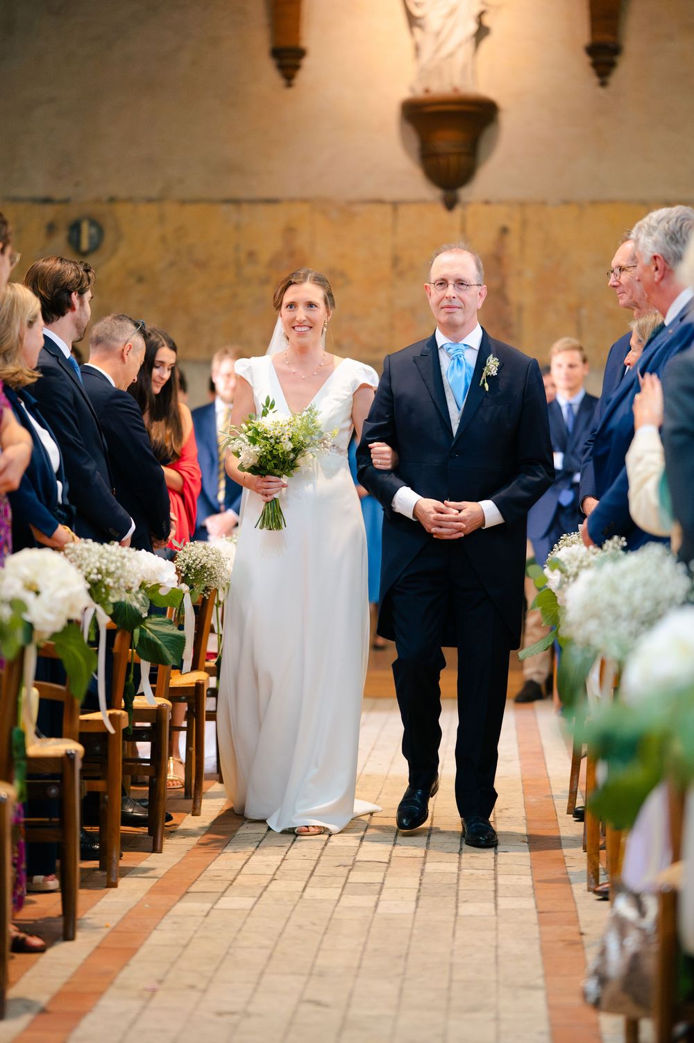 Wedding ceremony aisle decorated with floral arrangements and guests seated in wooden pews in a traditional church setting.