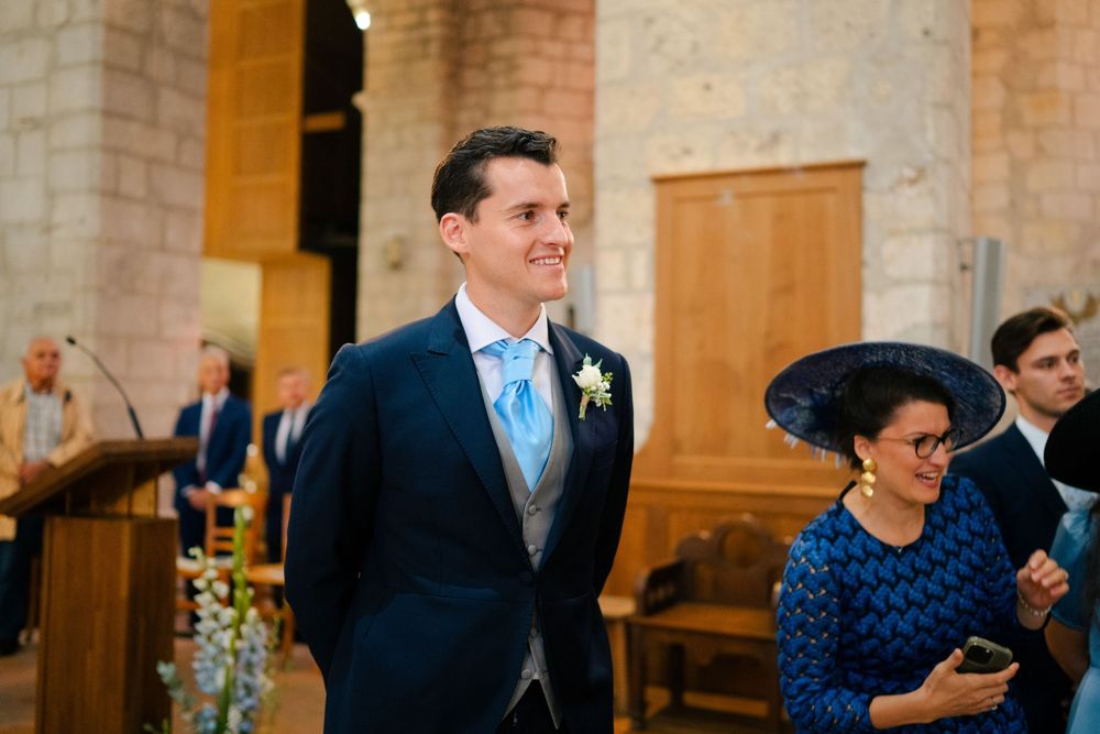 A wedding ceremony in a church with someone wearing a navy suit and light blue tie standing at the altar.