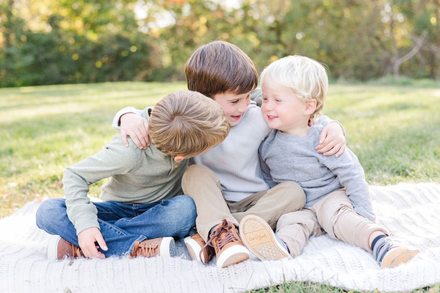 Family lying together on white blanket in grassy field during golden hour.