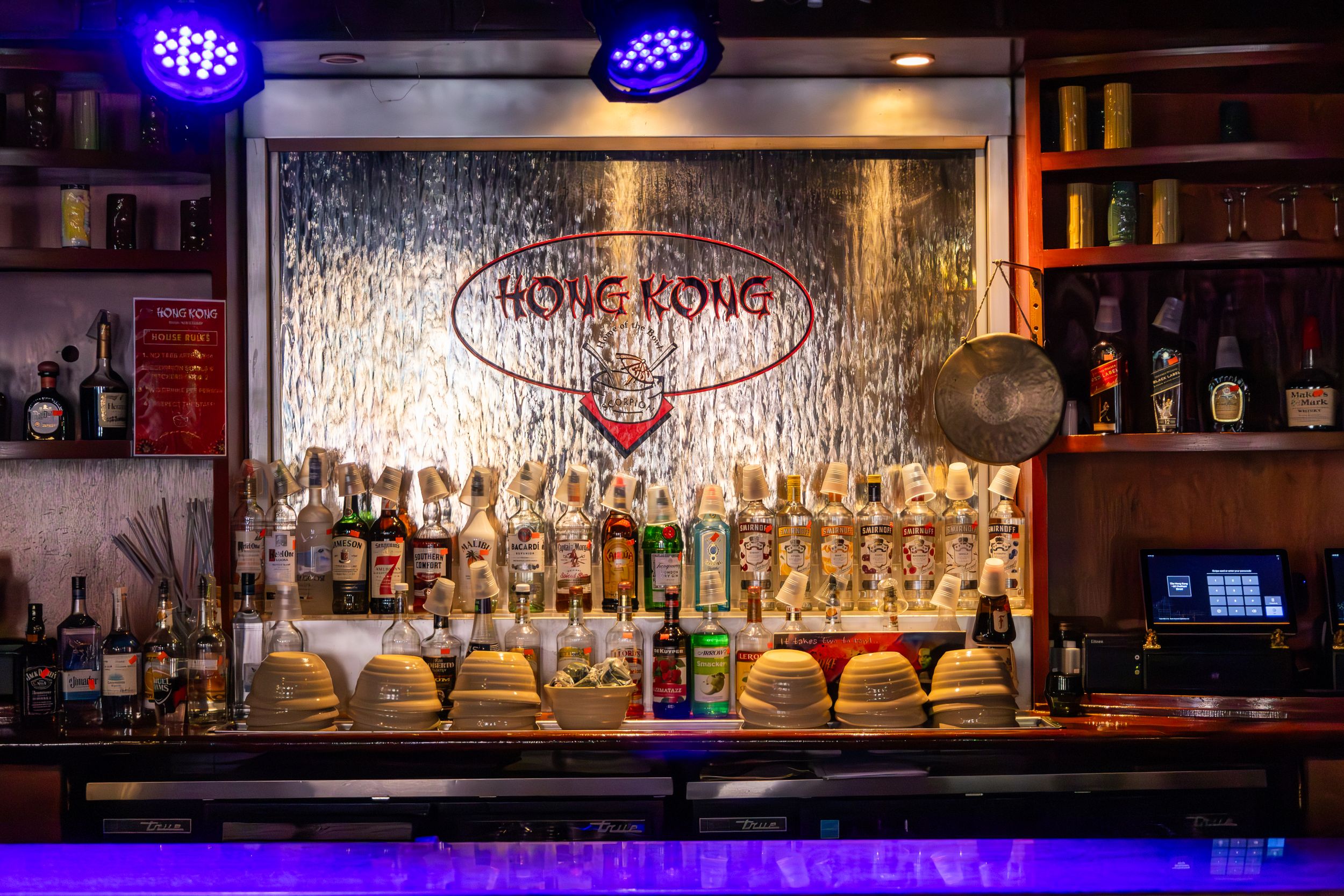 Illuminated bar display with Hong Kong neon sign and rows of liquor bottles.