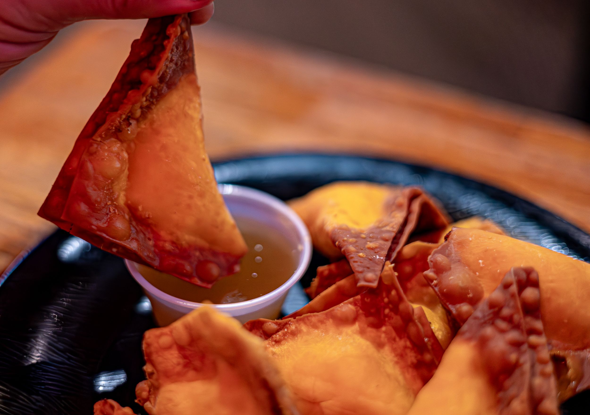 Golden fried wontons served with dipping sauce on a dark plate.