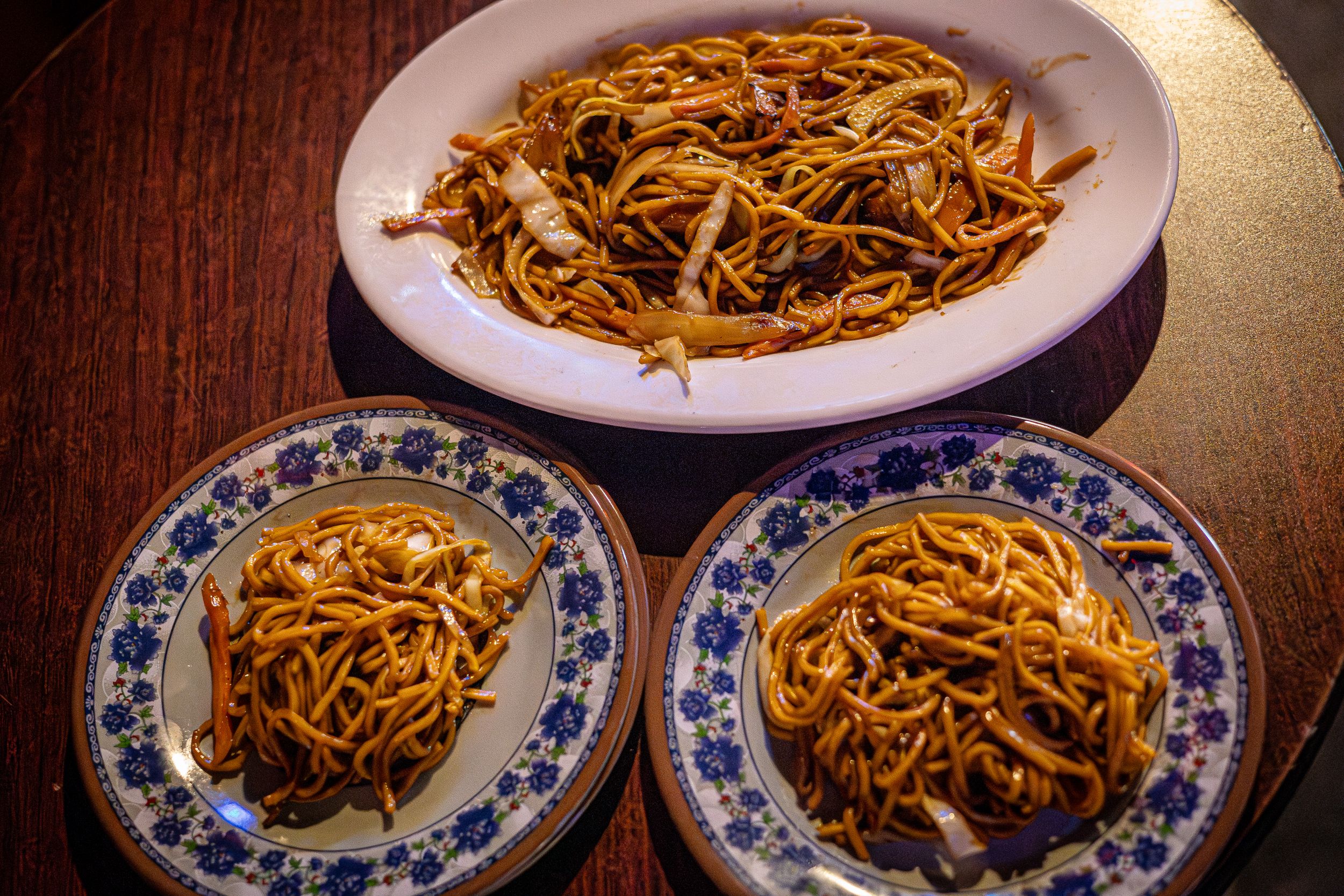 Three plates of lo mein noodles served on blue and white patterned china.