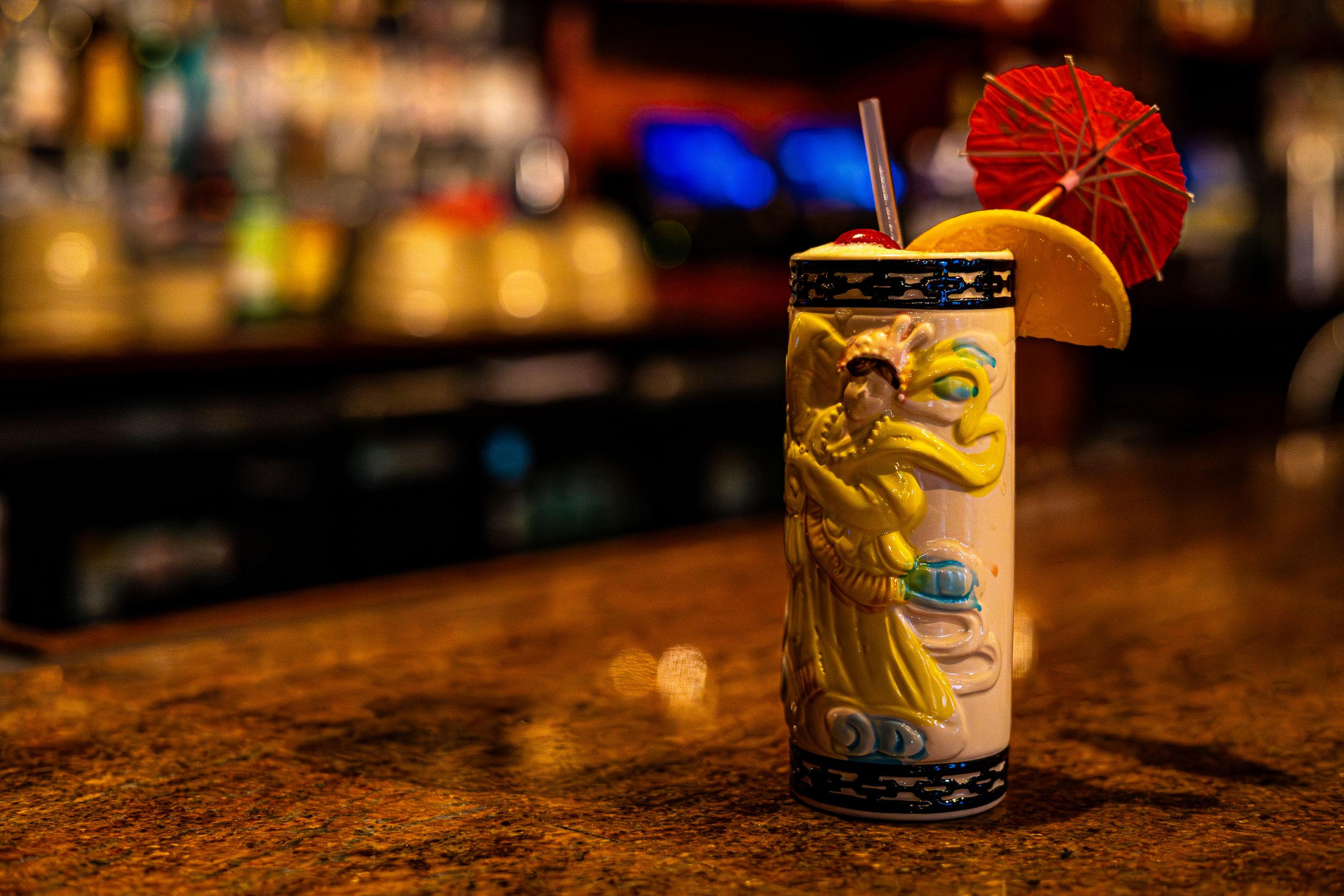Tropical tiki cocktail with umbrella garnish on wooden bar counter.