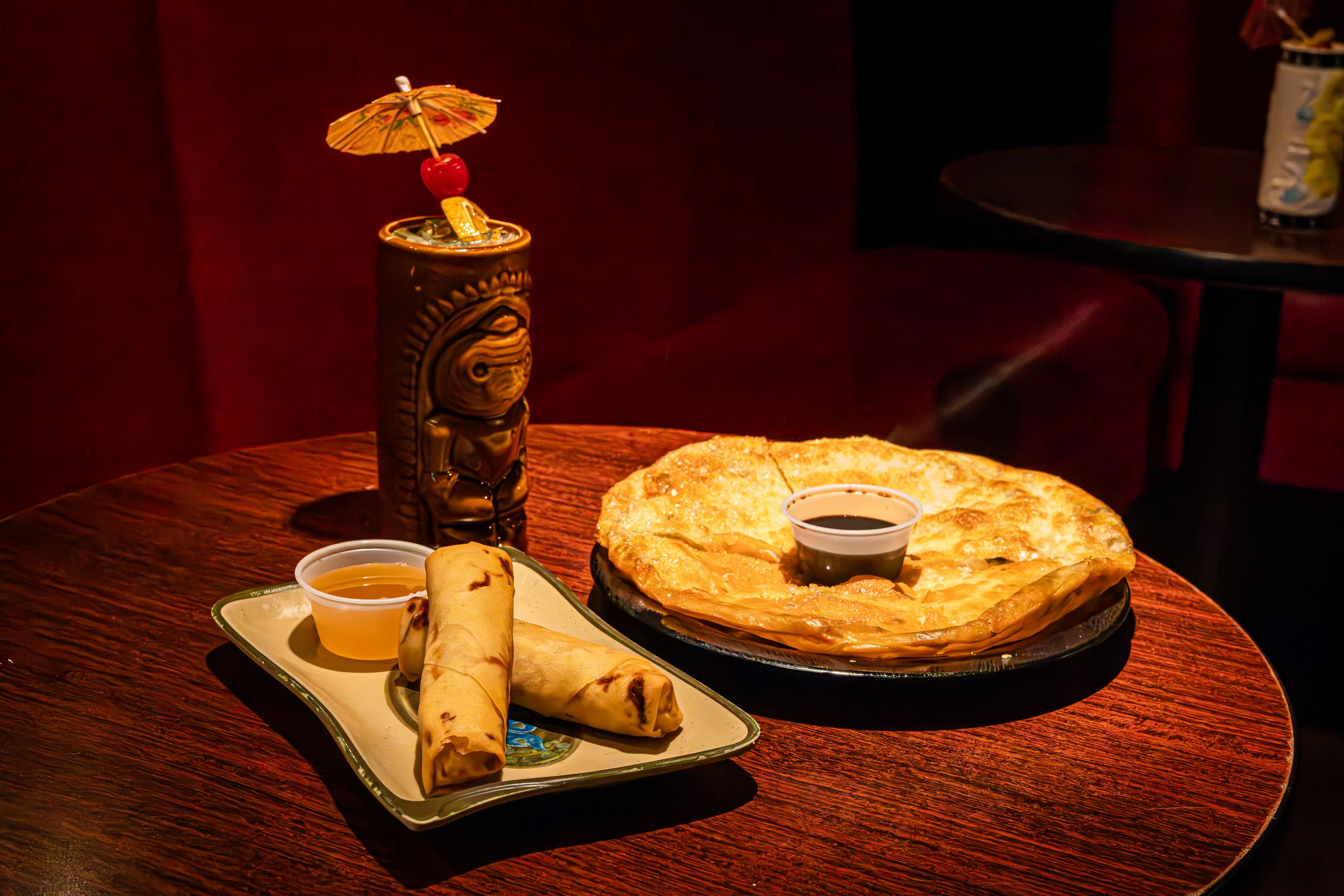 Spring rolls and scallion pancake served with dipping sauce on wooden table.