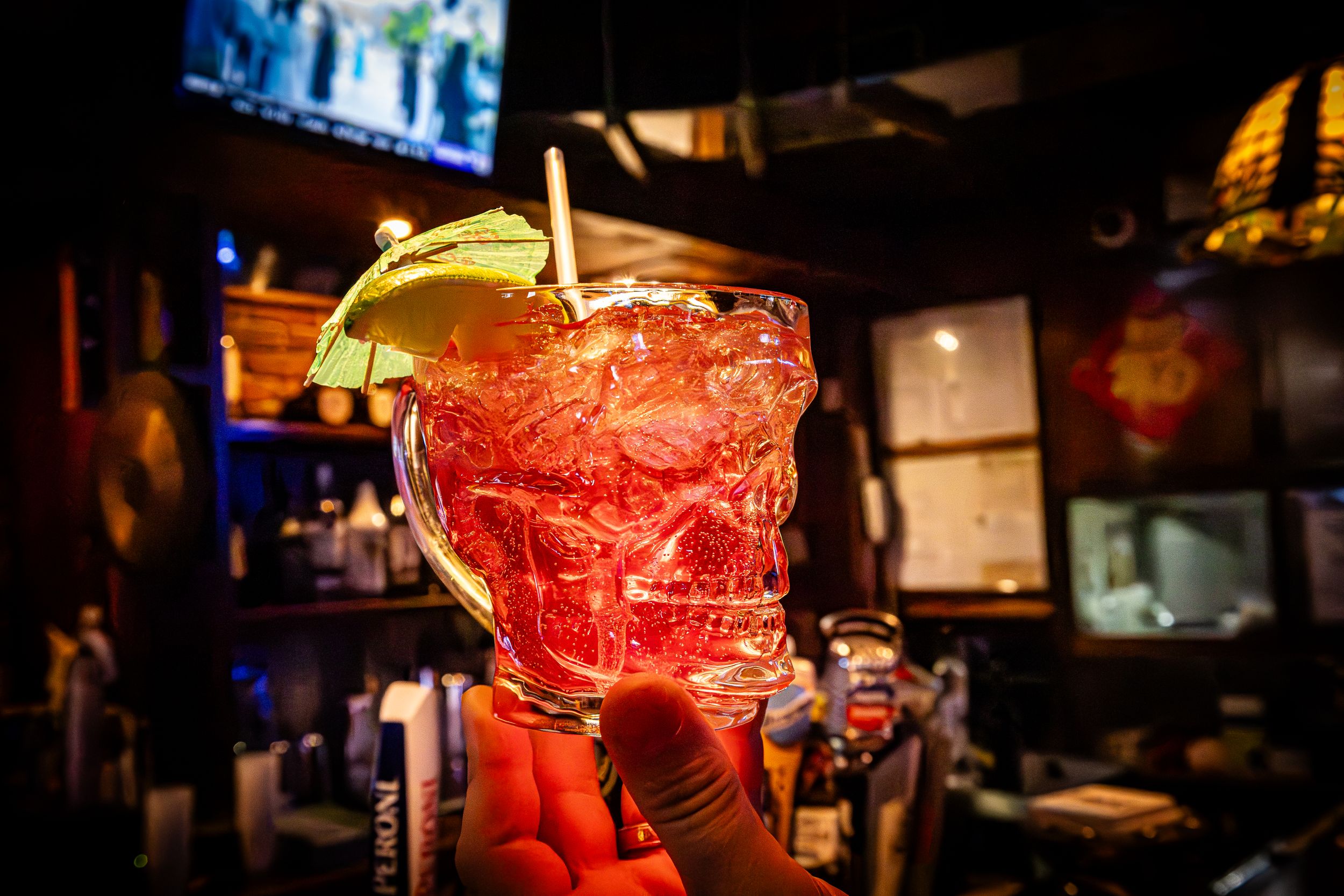 Red cocktail garnished with lemon slice in dimly lit bar setting.