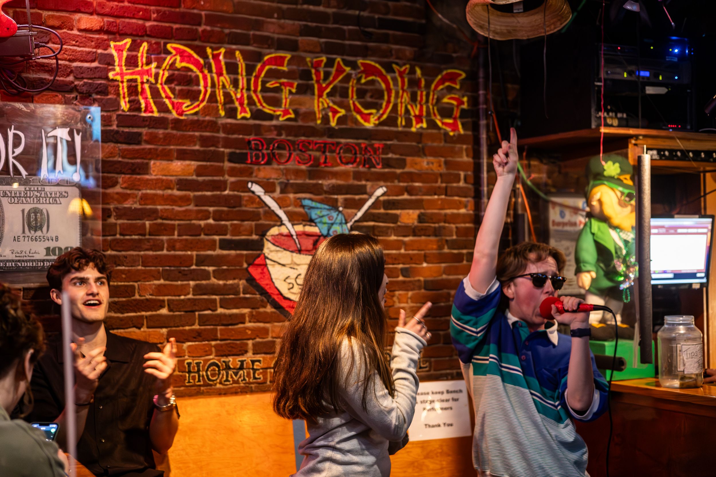 People celebrating at Hong Kong-themed bar with neon signs and drinks.