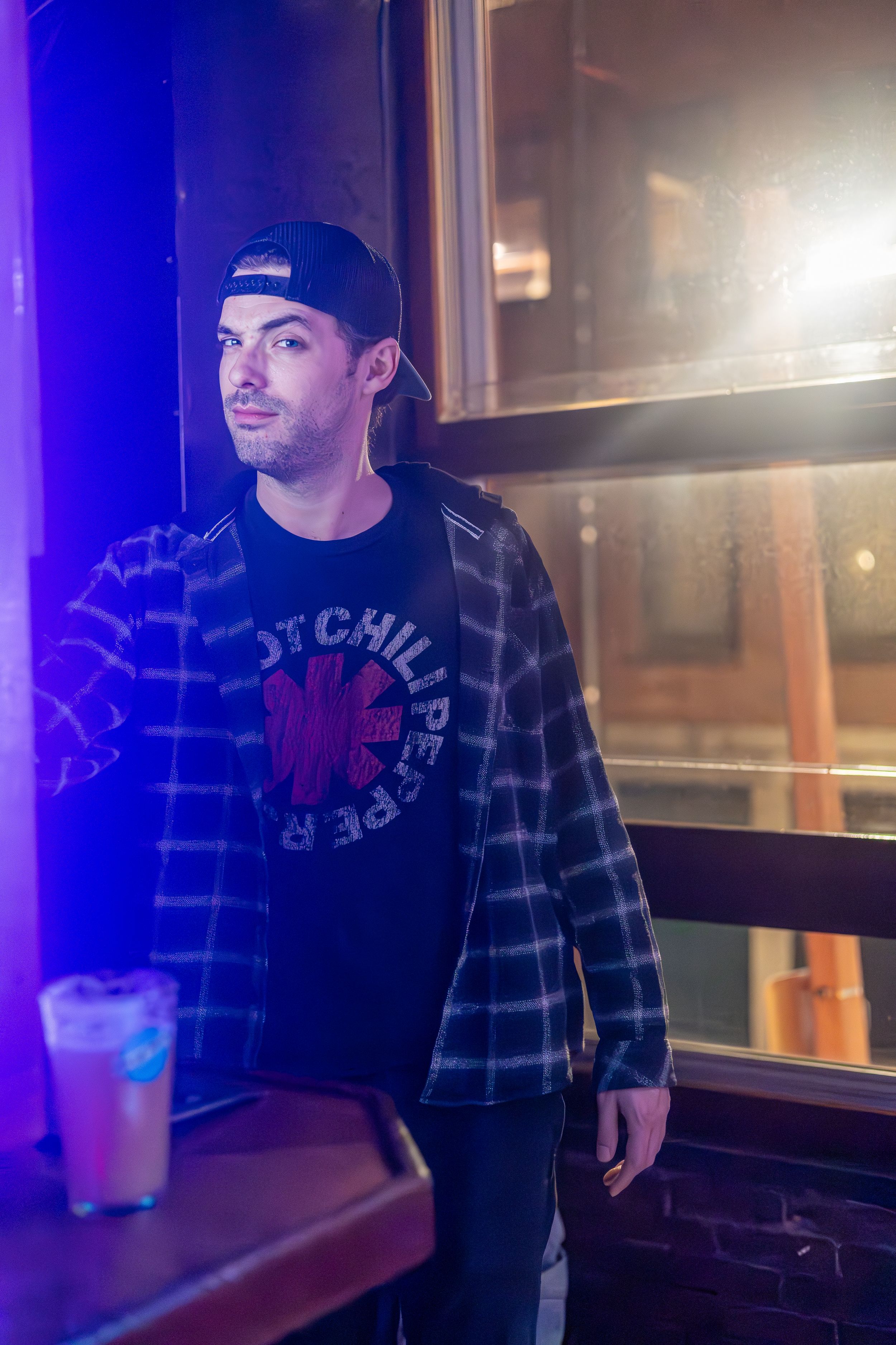 Casual patron in plaid shirt and baseball cap at a dimly lit bar.