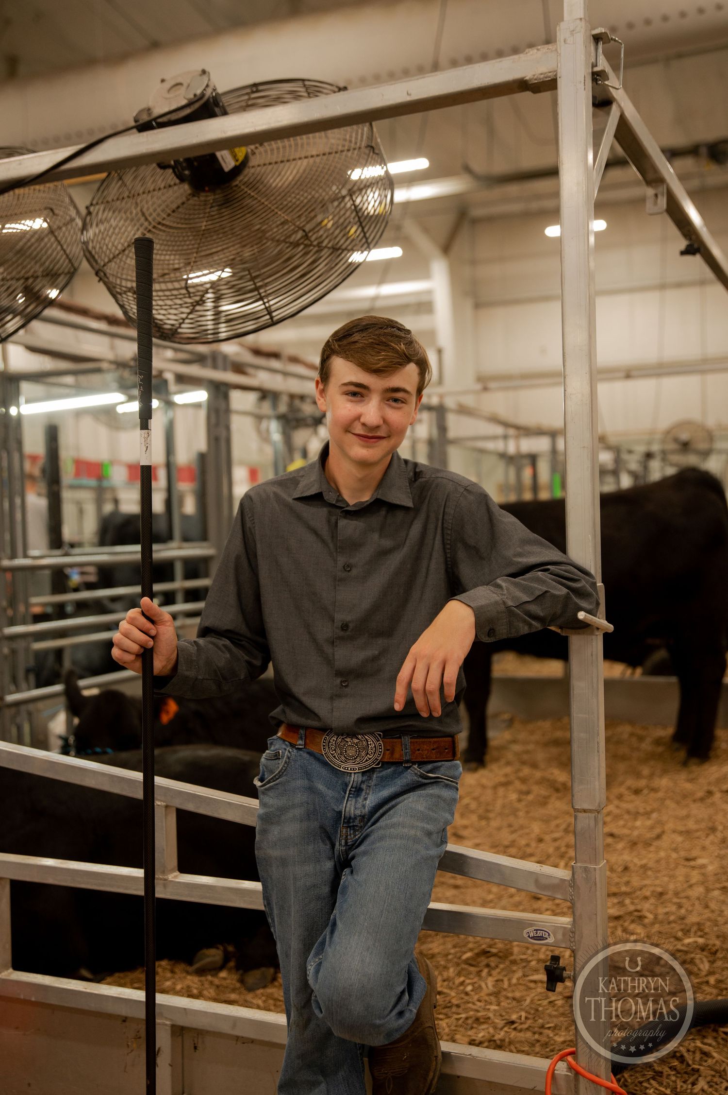 An exhibitor poses inside a modern livestock barn with industrial fans and metal gates visible.