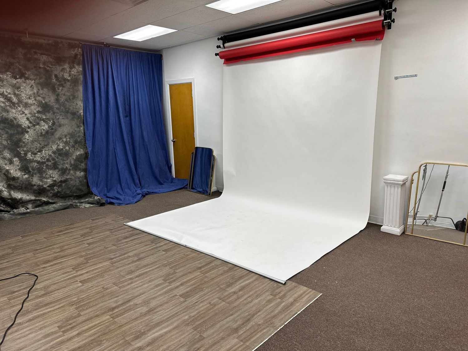 Professional photo studio setup with white backdrop, blue curtain and wooden floor.