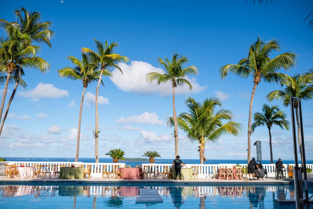 Palm trees line a pristine swimming pool against a bright blue Caribbean sky.