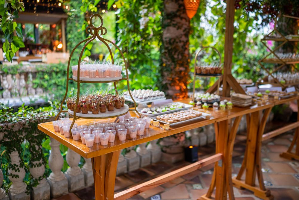 Glass serving ware displayed on wooden table in garden setting with hanging greenery.