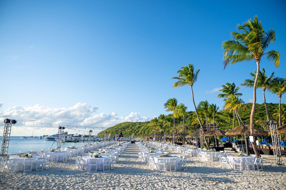 Palm tree lined beach with white chairs and tables set up for an oceanfront event.