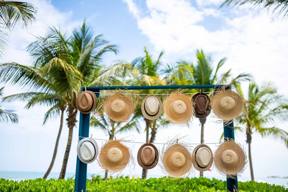 Row of straw sun hats hanging on display against a tropical palm tree backdrop.