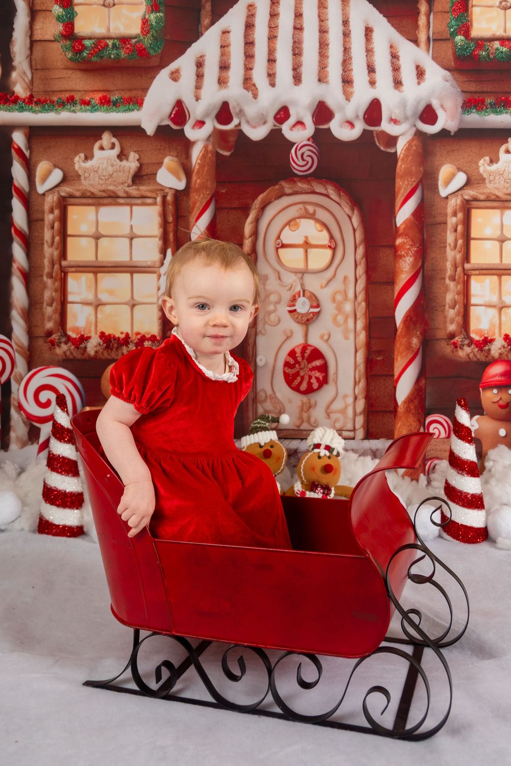 Festive holiday photo setup with decorative gingerbread house backdrop and red sleigh prop.