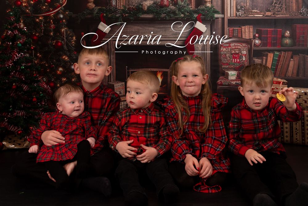 Group of children wearing matching red plaid outfits pose for Christmas portrait.