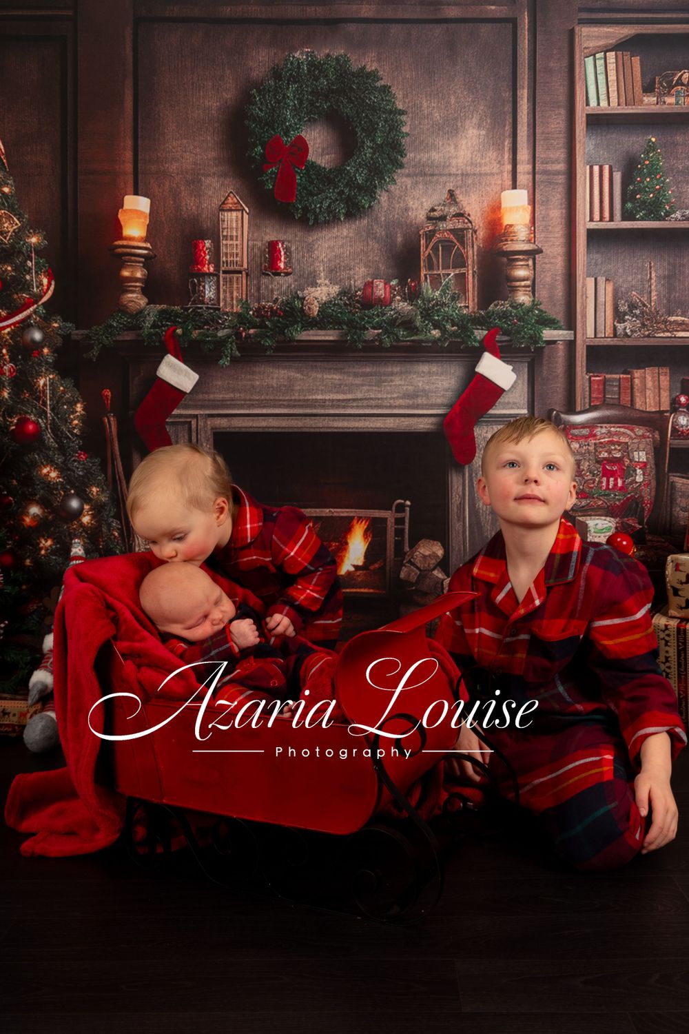 Three children in red plaid pajamas pose in front of a decorated Christmas fireplace setting.