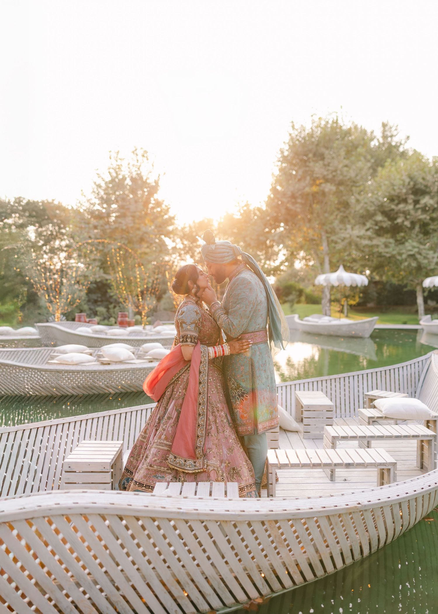 A beach wedding setup with crystal chandeliers and draped fabric over a couple in traditional Indian attire.