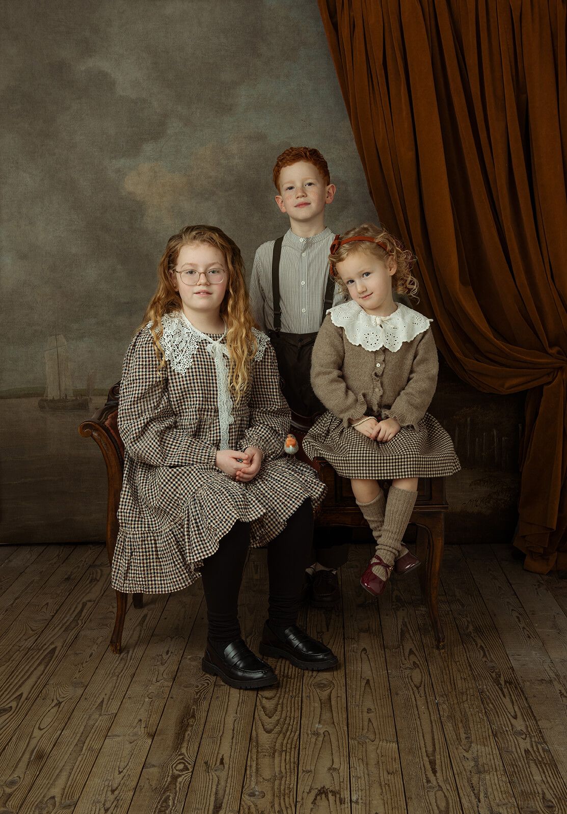 fine-art portret van twee zusjes en een broer met nette vintage kleding en rood gordijn op de achtergrond.